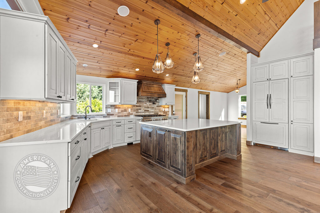 Kitchen with wood beam ceilings, white cabinets, island by American Construction Services, Corp.