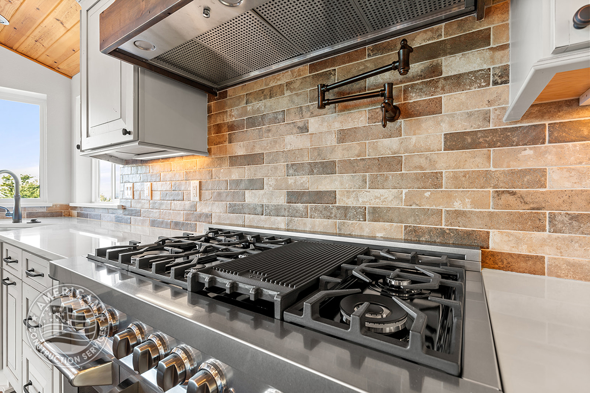 stainless steel cooktop with hood, backsplash, and pot filler in kitchen remodeled by American Construction Services, Corp.