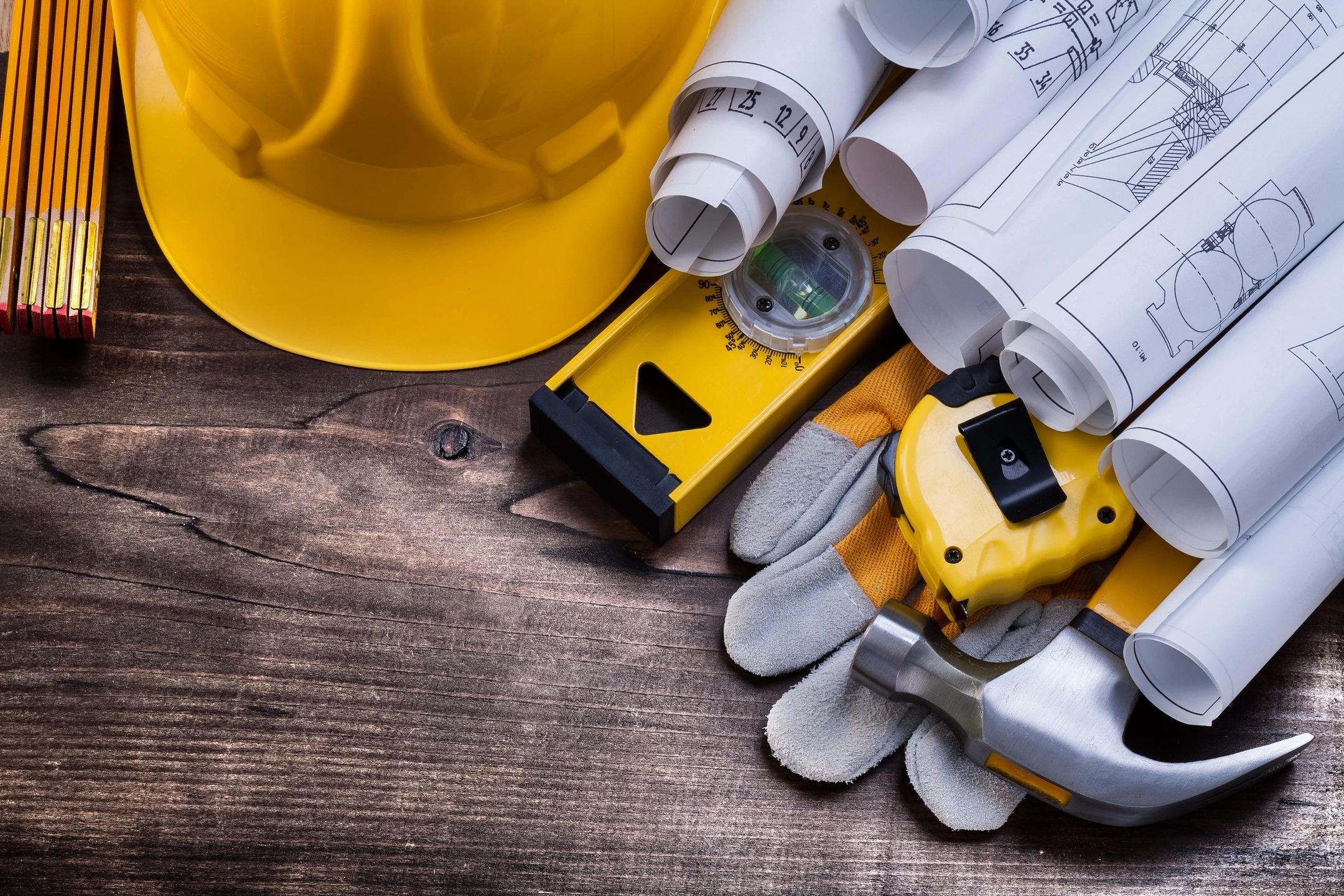 Hard hat, level, gloves, and blueprints on a wooden background